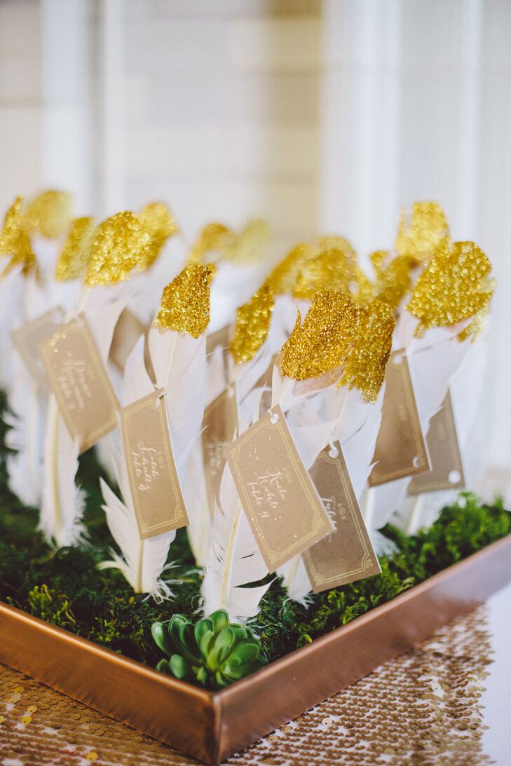 The DIY escort cards were each tied to a gold glitter-dipped white feather stuck in floral foam boards covered in moss and succulents. “It was one of my favorite things we made for the wedding!” says the bride.