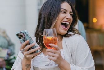 Woman holding drink and phone in her hands while laughing 