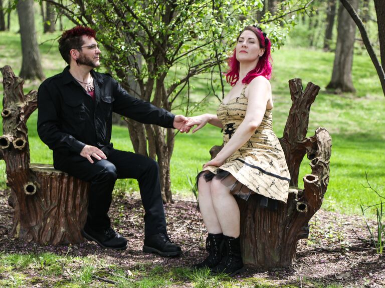 Couple poses for the camera while sitting on tree stumps. 