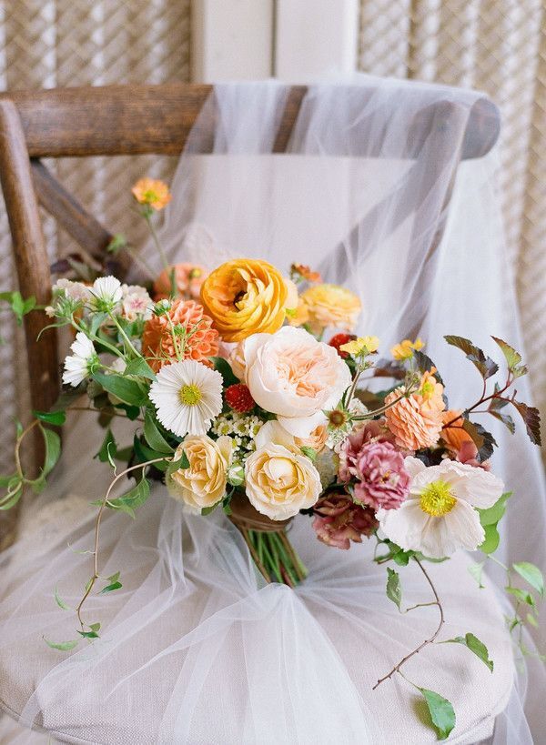 Orange wedding bouquet sitting on chair with veil