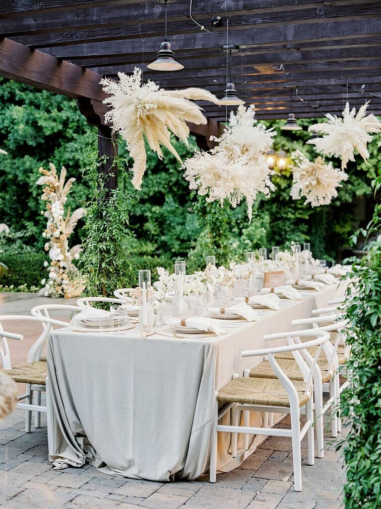 outdoor wedding reception with clusters of white pampas grass hanging above long banquet table