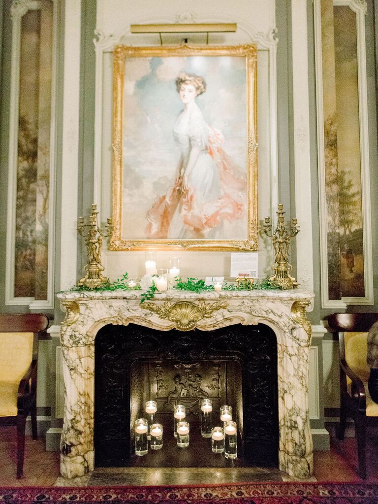 elegant wedding fireplace with marble and gold carved mantel, antique oil painting and simple greenery with votive candles