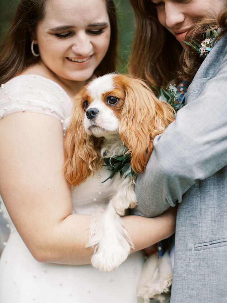 A bride and groom hold their dog of honor, a Cavalier King Charles Spaniel named Lady, who's wearing a floral collar.