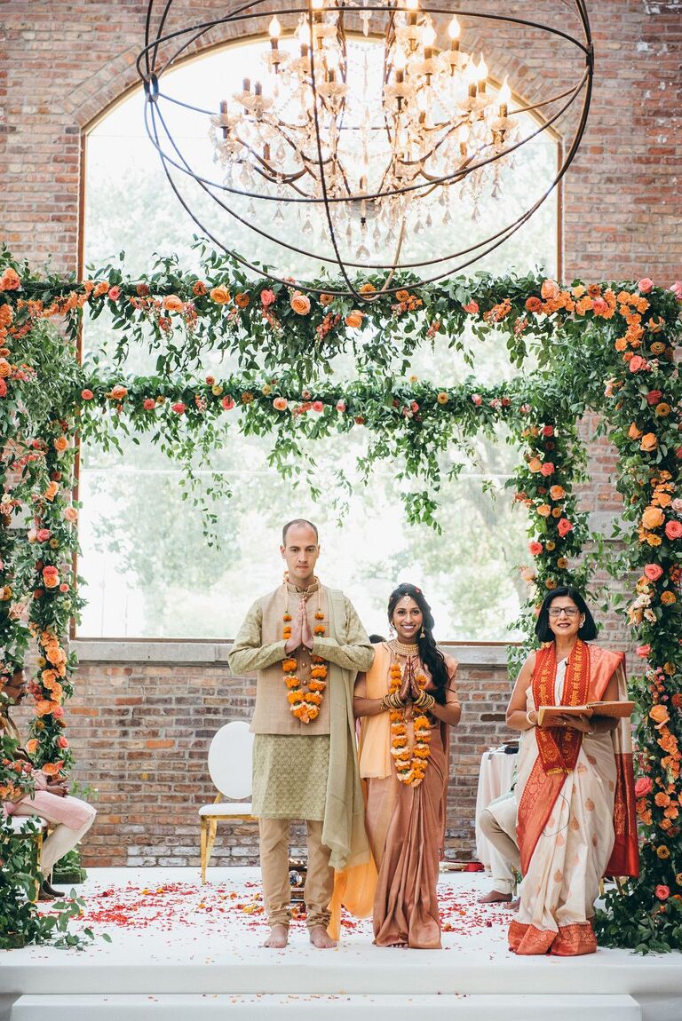 Couple standing under green-and-orange mandap