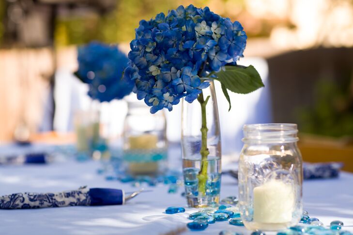 At the reception, dining tables were decorated with small blue stones scattered across the linens. Blue hydrangeas purchased from a local market were placed in simple glass vases, which alternated as table centerpieces with candles in glass mason jars.