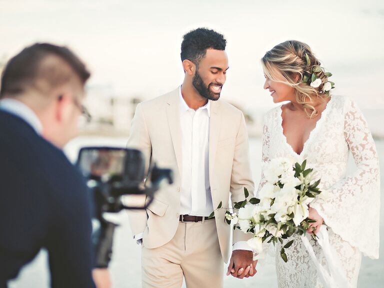 Bride and groom smile at each other while videographer takes footage. 