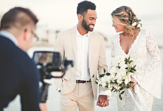Bride and groom smile at each other while videographer takes footage. 