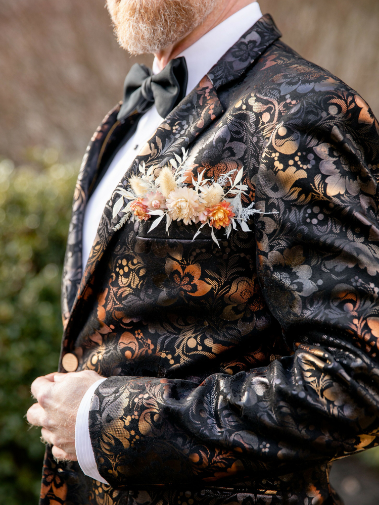 Groom wearing ornate suit jacket with flowers in breast pocket