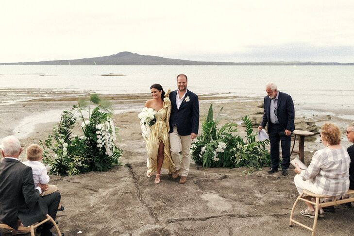 Bride in Gold Metallic Dress, Groom in Casual Suit at City Beach Ceremony, Foliage Altar