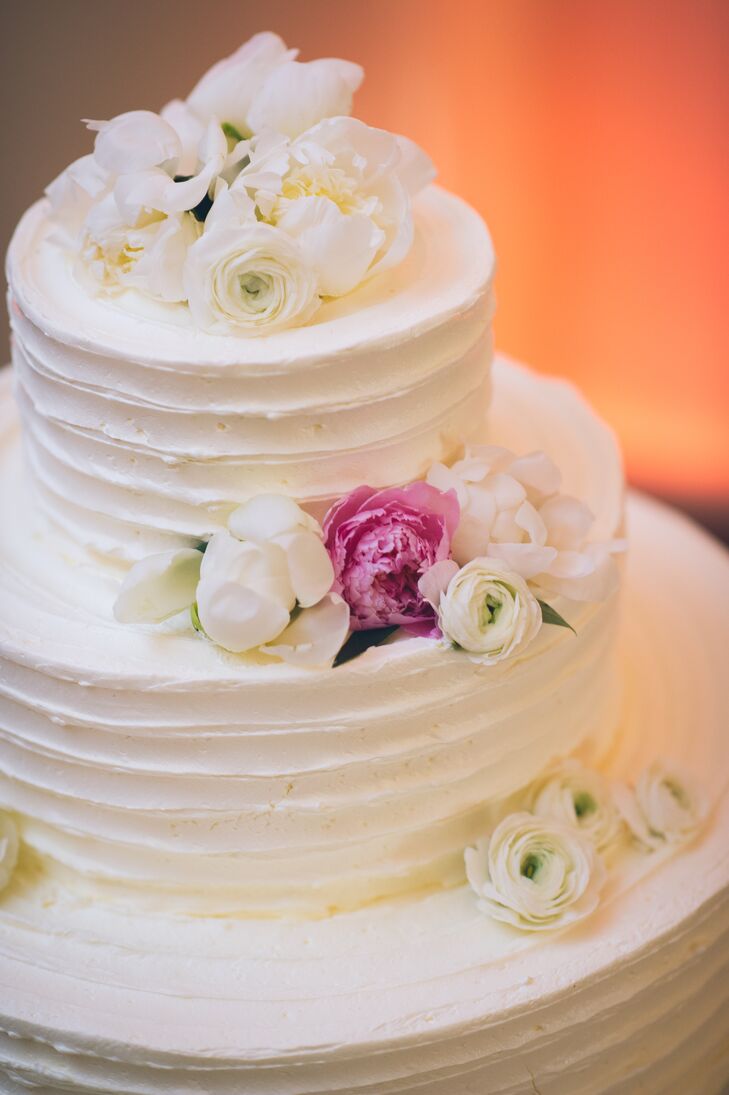 Every layer of their wedding cake corresponded with the couple’s romantic centerpieces. Creative Cakes By Donna covered each round tier with white buttercream frosting below fresh flowers. White and pink peonies as well as white ranunculus and slight green leaves peaked out of either side or a natural design.