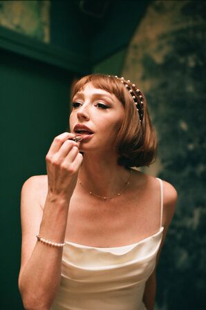 Bride With Short Hairstyle, Pearl Headband and Spaghetti-Strap Dress Puts on Lipstick, Glam Makeup