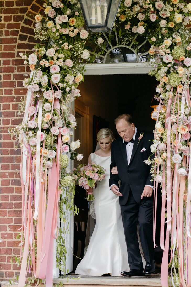 Bride and Father of the Bride Walking Through Doorway Covered in Roses and Ribbons