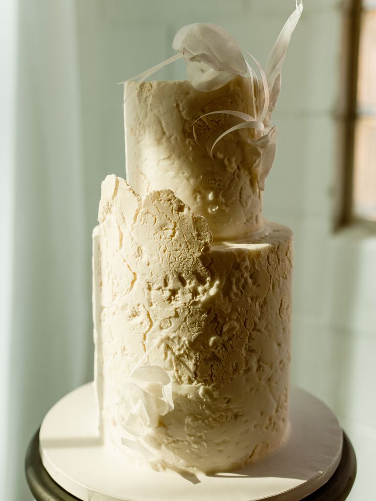 modern two tier wedding cake with ivory textured buttercream and feather accents