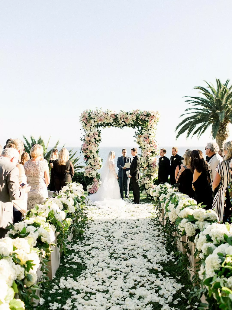 A wedding aisle lies strewn with romantic white rose petals.