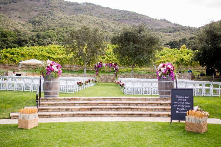 Fitting with the vineyard setting, a pair of wine barrels topped with cascading floral arrangements sat at the ceremony entrance. Purple and ivory blossoms were placed on wrought-iron hooks down the aisle leading to the wedding arch.
