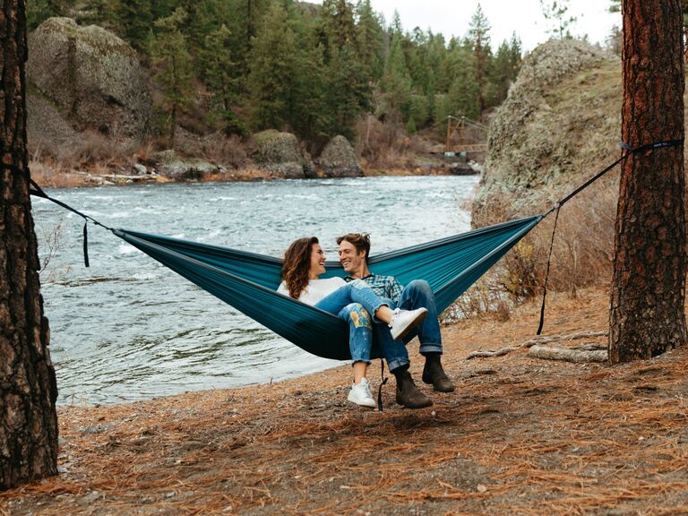 Couple relaxes on a hammock near a river. 