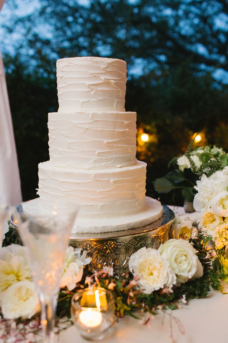 Lindsey and Daniel's wedding cake was simple and classic: It had three round tiers covered in textured white buttercream atop a textured metallic gold cake stand. Ivory flowers and greenery surrounded the cake display. "It was important for the cake to feel like we made it at home," Lindsey says.