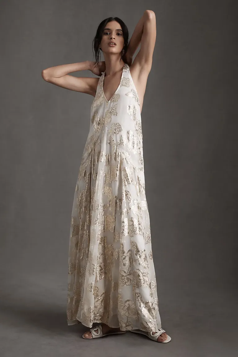 Model wears a floor-length gown with a halter neckline and gold detailing. 