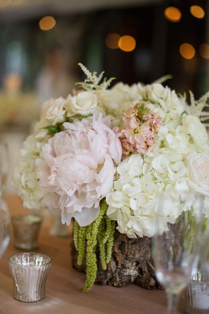 Low centerpiece arrangements of white hydrangea, blush garden roses, peonies, sahara roses, hanging green amaranths and pops of pale peach stock sat on rustic wood slabs.