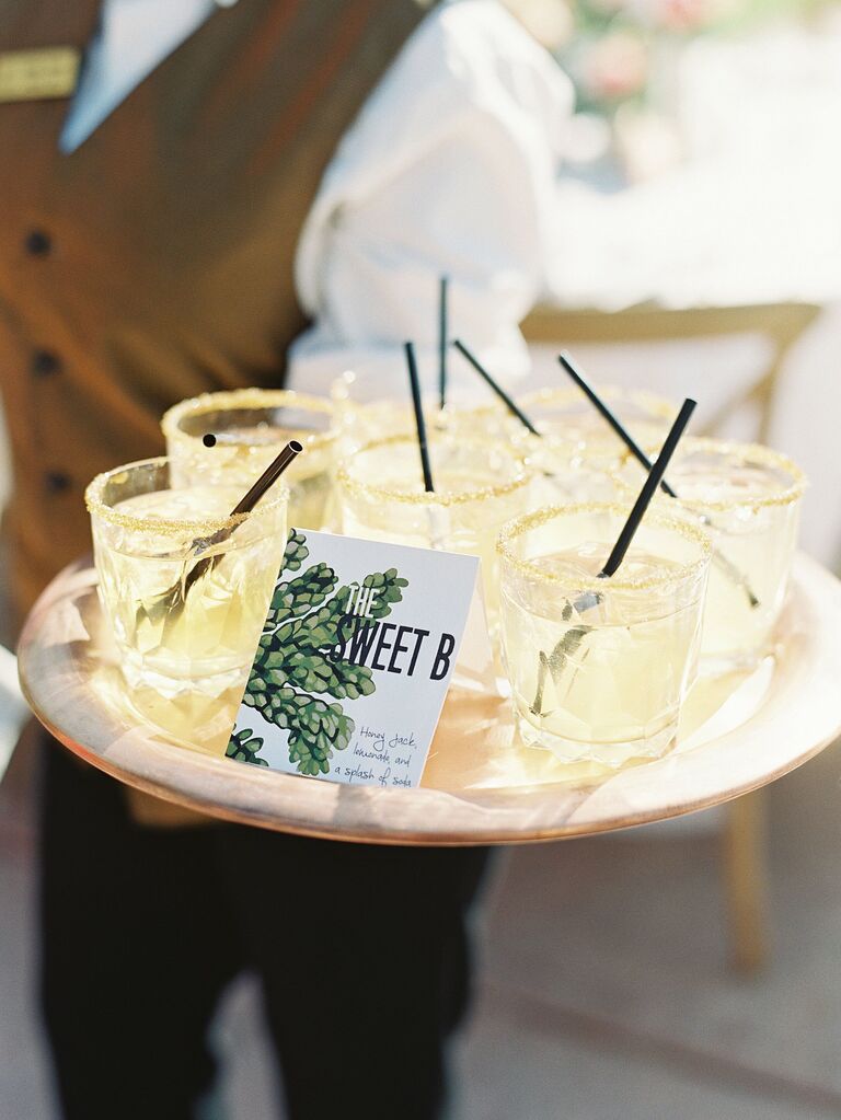 server holding a tray of light yellow colored drinks with black straws