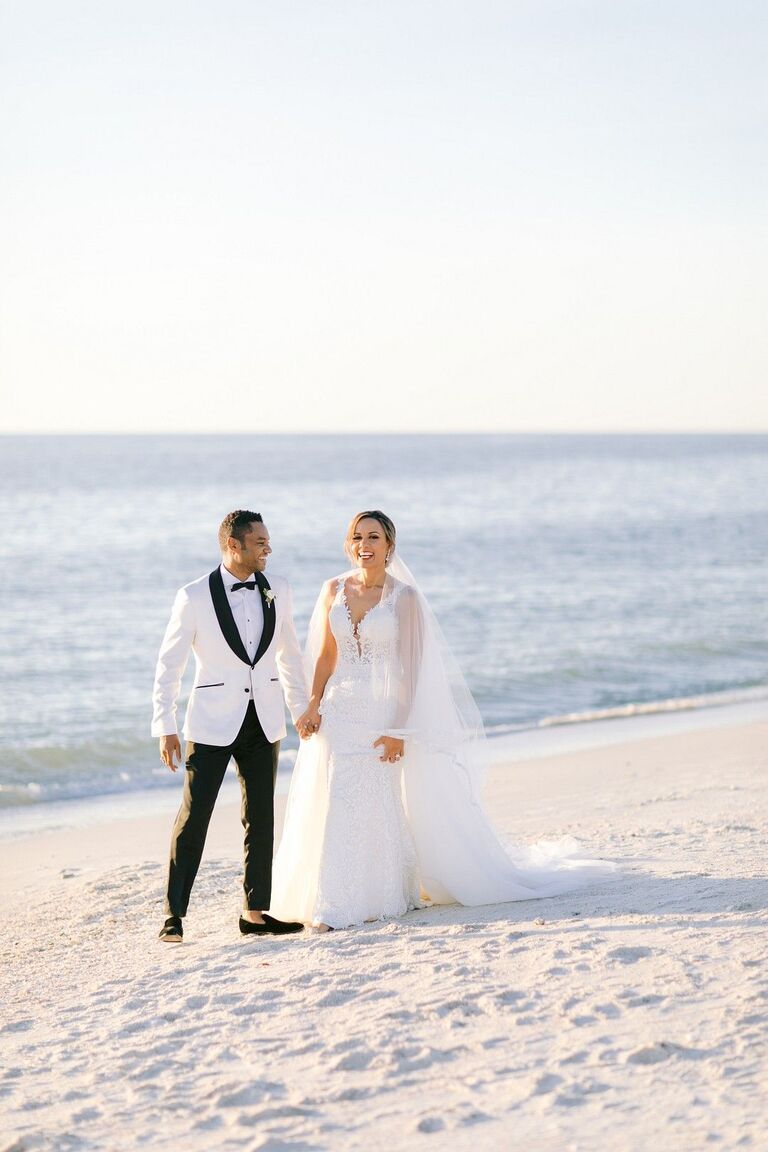 Couple in black-tie attire holding hands on the beach