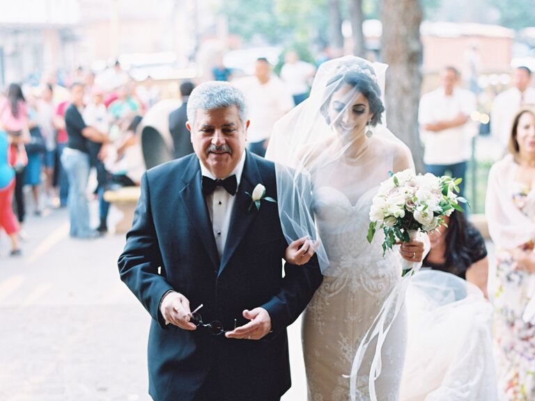 A bride is lead down the aisle holding her bouquet.
