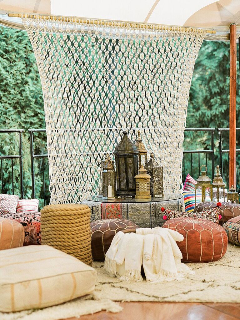 Moroccan-themed seating area inside tented wedding with couches, blankets and poufs