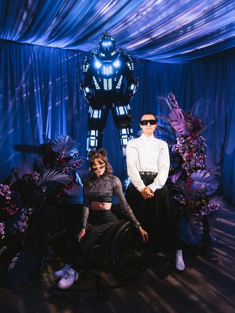 couple dressed in futuristic attire posing with LED stiltwalker robot