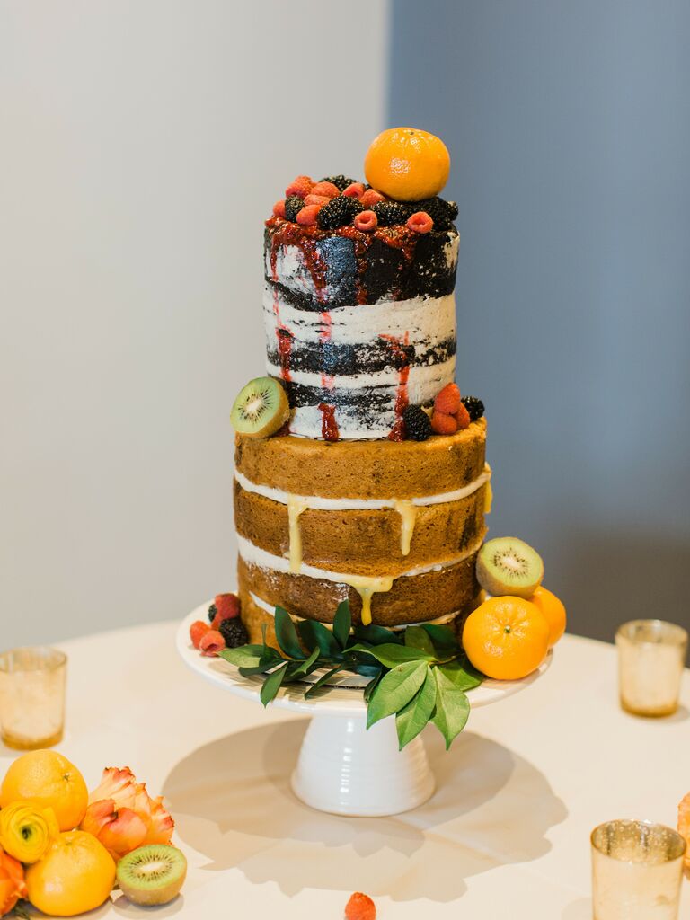 two tier naked wedding cake with sliced kiwis, fresh berries and clementines