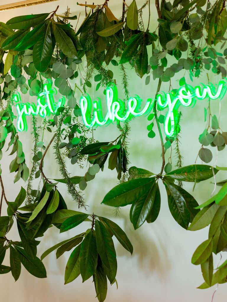 green neon wedding sign hanging against a curtain of fresh greenery and leaves