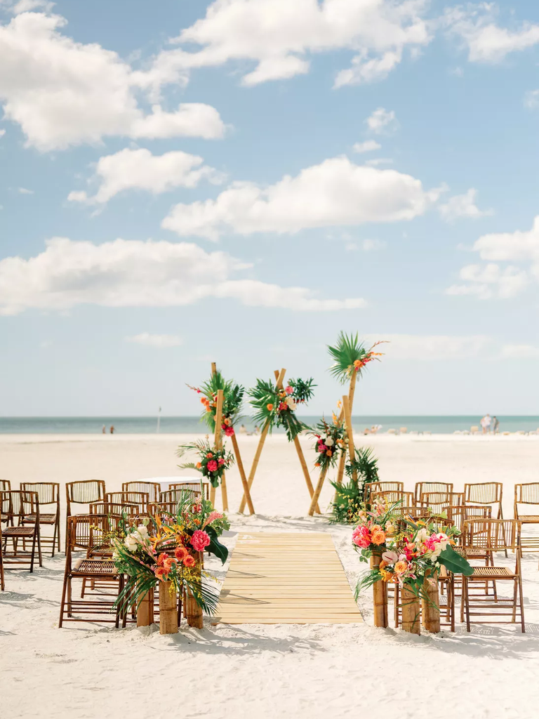 Three triangular shapes create a modern geometric wedding arch on the beach.