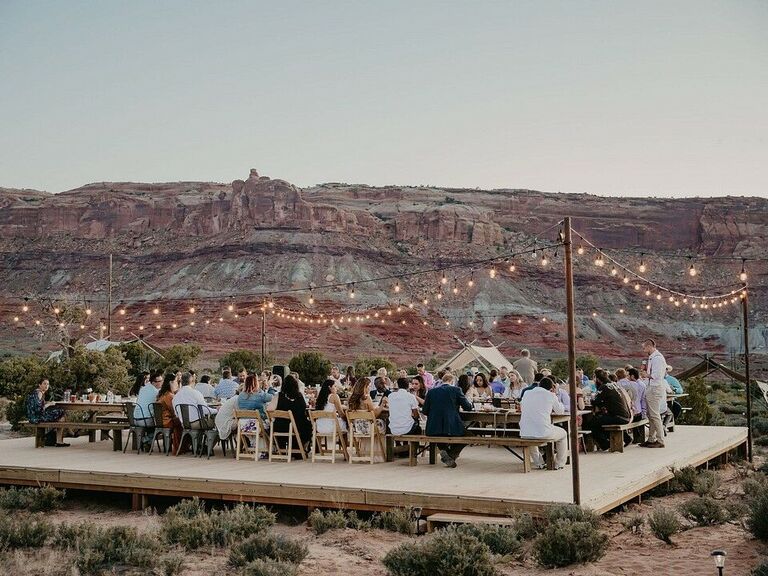 outdoor wedding reception taking place in the desert with string lights surrounding guest tables on a wooden platform