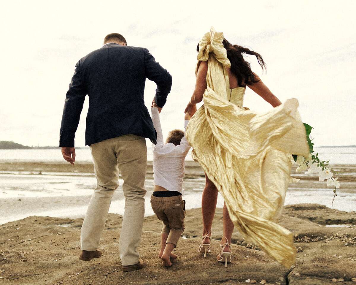 Bride in Gold Metallic Dress, Groom in Casual Suit and Young Son Holding  Hands on Beach