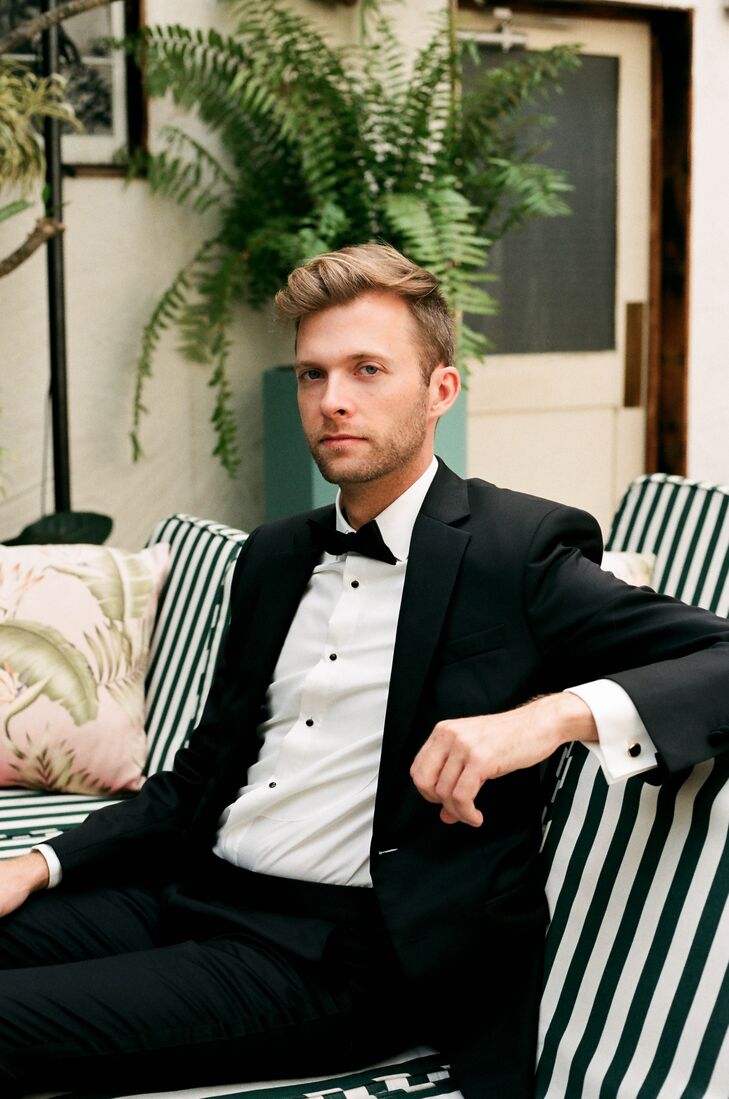 Groom in Classic Black Tuxedo and Bow Tie Posing on Striped Couch