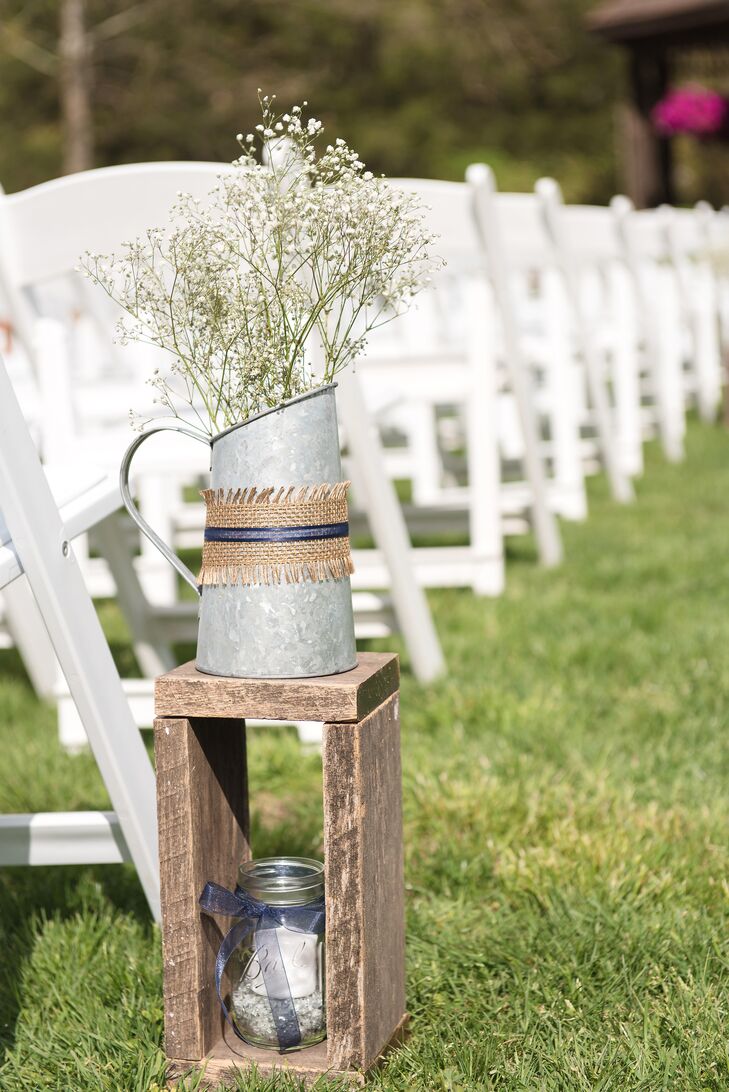 “It was pretty much love at first sight,”  Rachael says. “He was the farmer and I was the country horse girl.” With this in mind, they included a few country-inspired details in their wedding. The aisle was lined with these arrangements of baby’s breath inside galvanized watering cans. Each one was wrapped in burlap and navy ribbon as well as placed on a wooden stand.