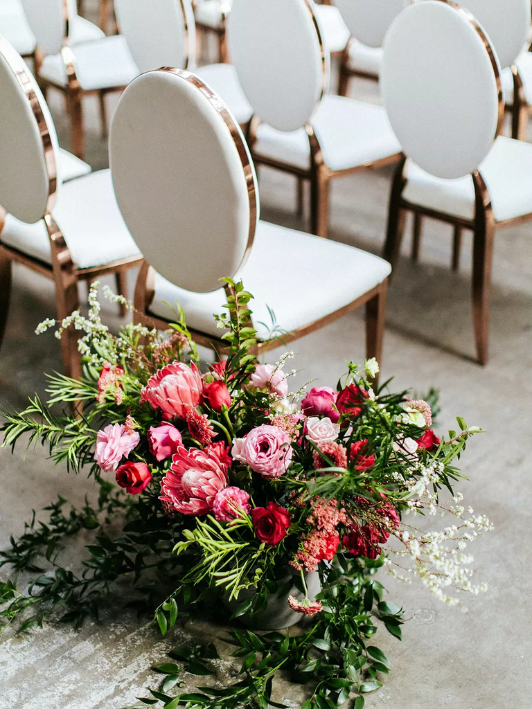 A vibrant pink floral arrangement sits beside elegant wedding chairs.
