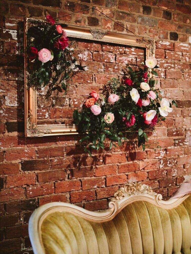 Empty vintage picture frame hanging on exposed brick wall with clusters of flowers