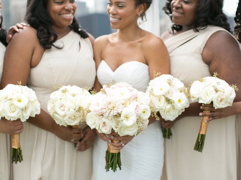 A bride and her wedding party holds white rose bouquets.