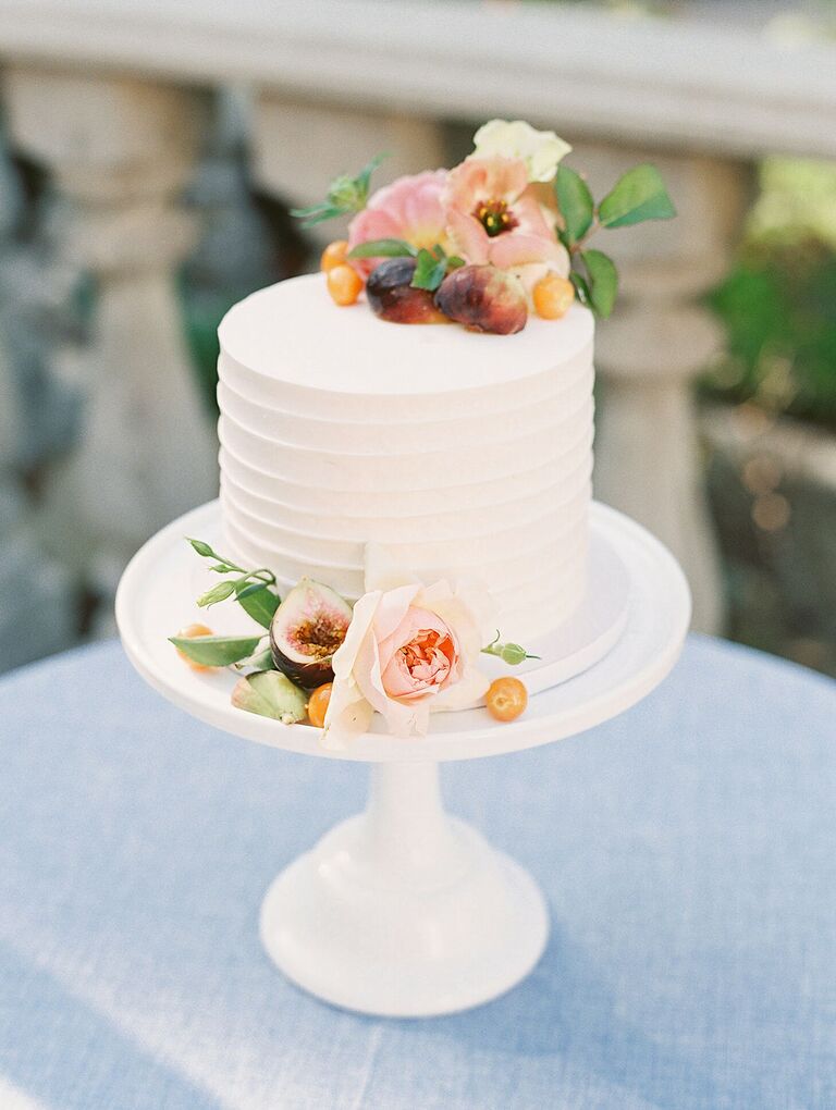 One-tier cake on white cake stand with fresh fruit and flower decorations