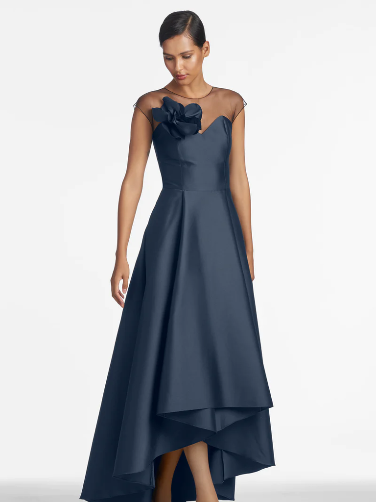 A model shows off this stunning asymmetrical gown with sheer shoulders and a statement flower.