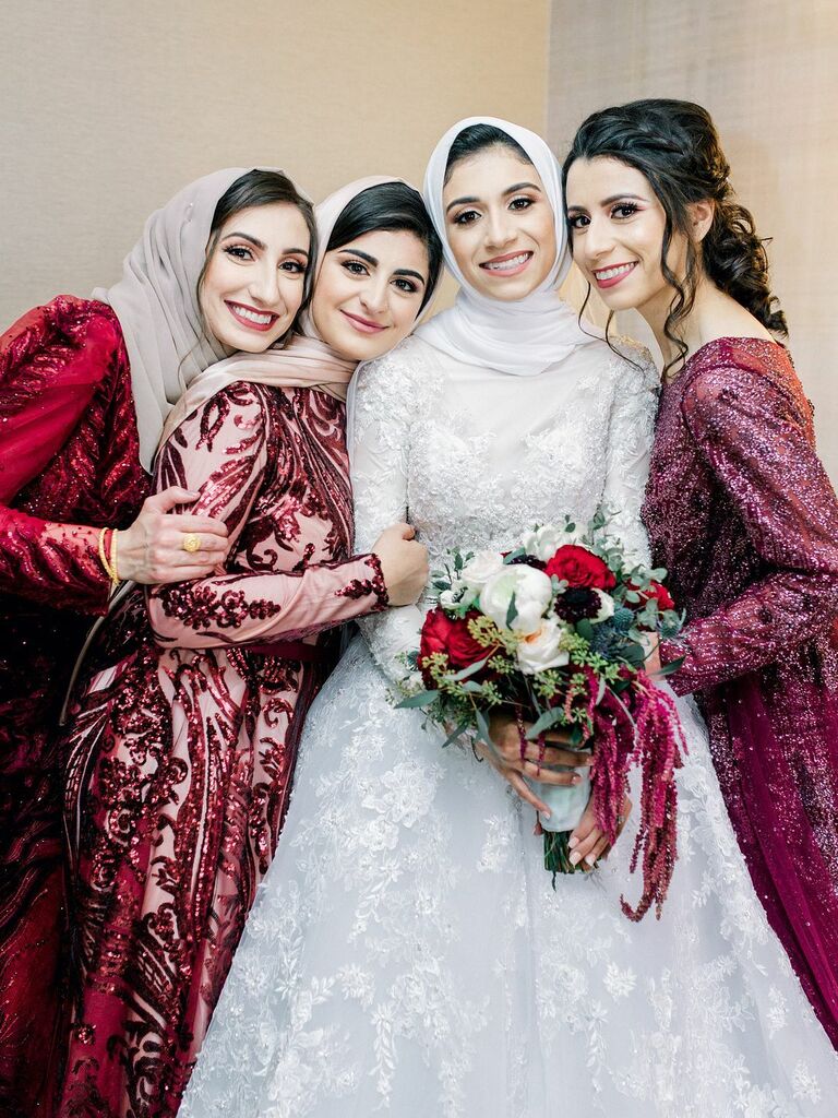 Bridesmaids wear embellished dresses in shades of red and pink. 
