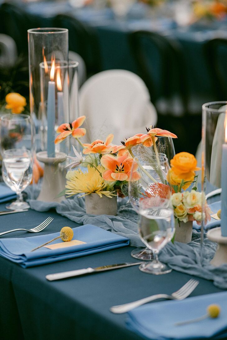 Table With Blue Linen, Napkins and Candles Accented By Orange and Yellow Flowers