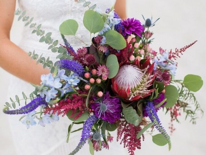 Bride holding purple bouquet with veronica and protea