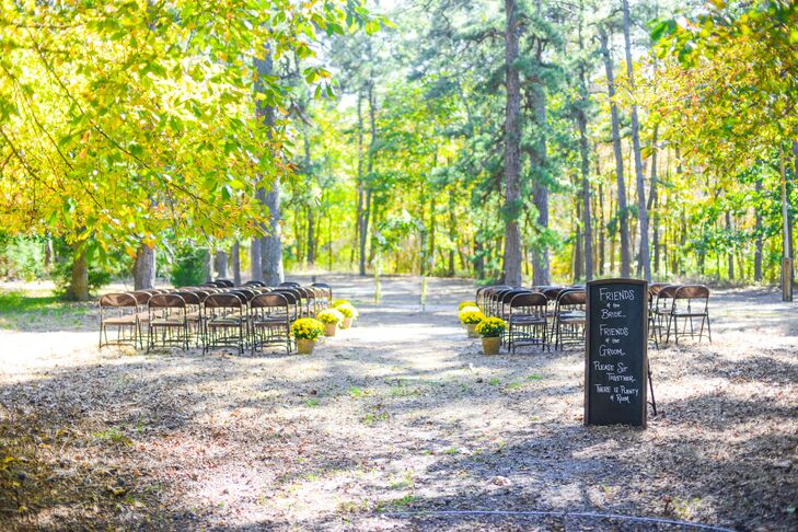 Stephanie and Michael's ceremony decor blended in with their surroundings. The couple highlighted each trunk and changing foliage with lines of dark folding chairs and potted yellow chrysanthemums. Michael even made their greenery-wrapped wedding arch for an even more personalized touch.