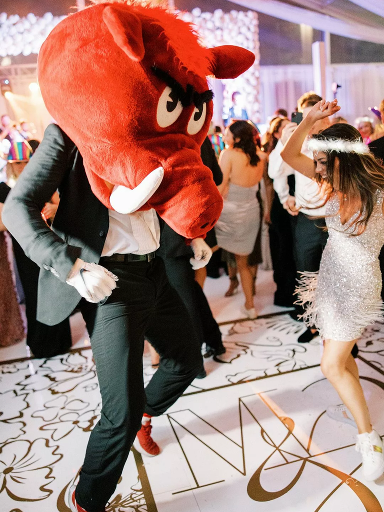 A bride dances with her groom, who wears a mascot mask in the shape of a hog.
