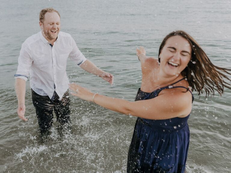 Couple splashes in the ocean during their engagement shoot. 