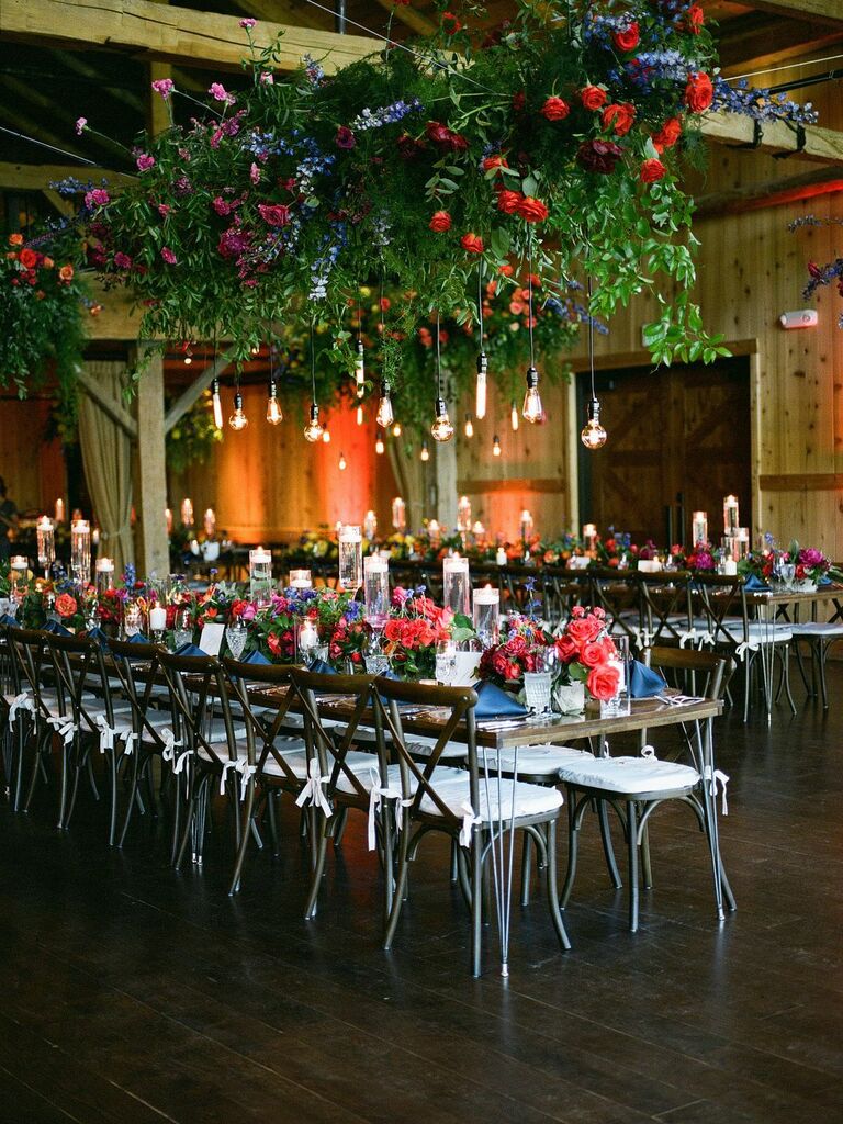 indoor wedding reception with hanging jewel tone purple blue and red flower centerpiece accented with edison bulbs on long cords 