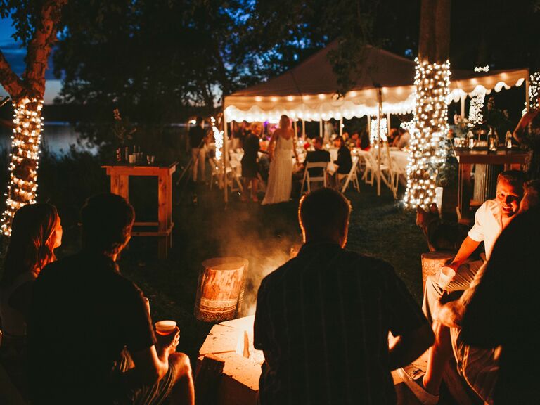 Group of people gathered around a bonfire outside a wedding. 