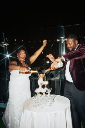 Bride and Groom Pouring Champagne on a Tower of Champagne Glasses on Rooftop