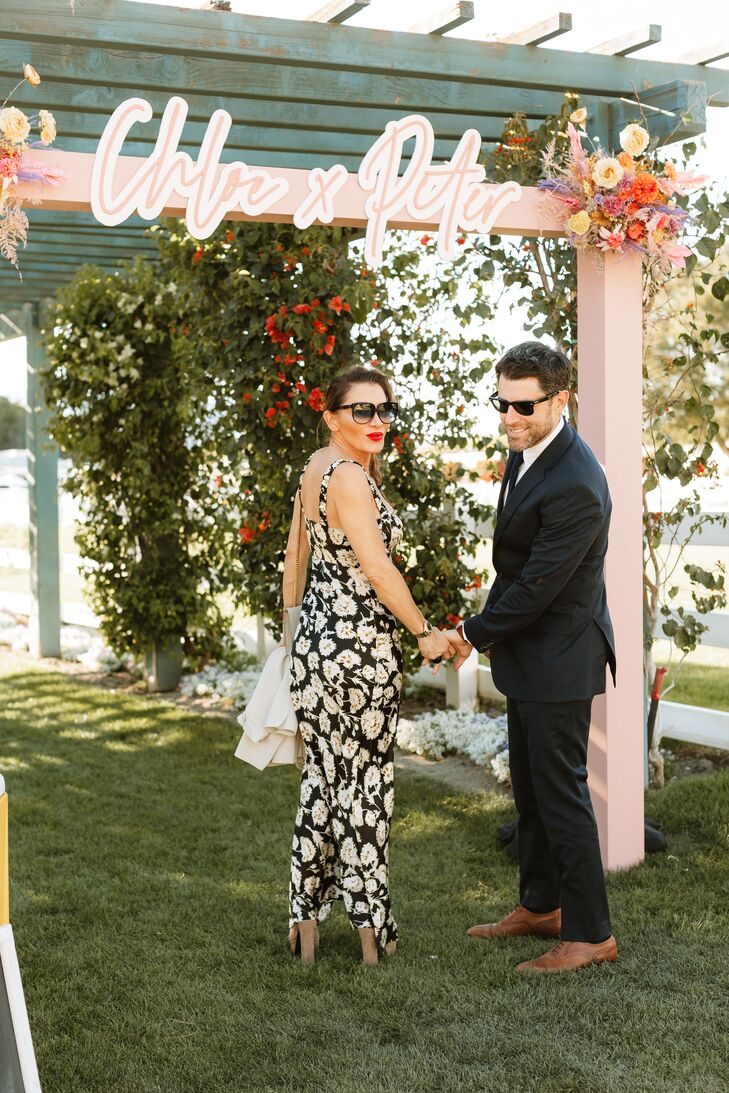 Actor Max Greenfield (New Girl) and his wife, Tess Sanchez, arriving at a retro desert wedding as guests in semi-formal attire and sunglasses.
